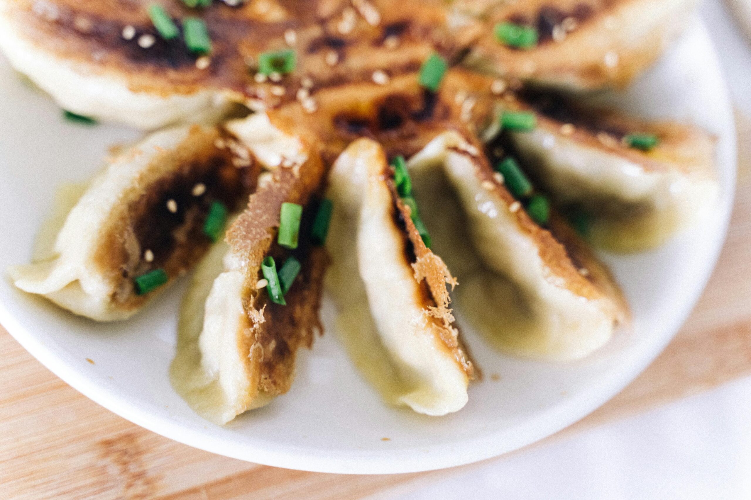 Delicious crispy pan-fried dumplings garnished with scallions and sesame seeds on a white plate.