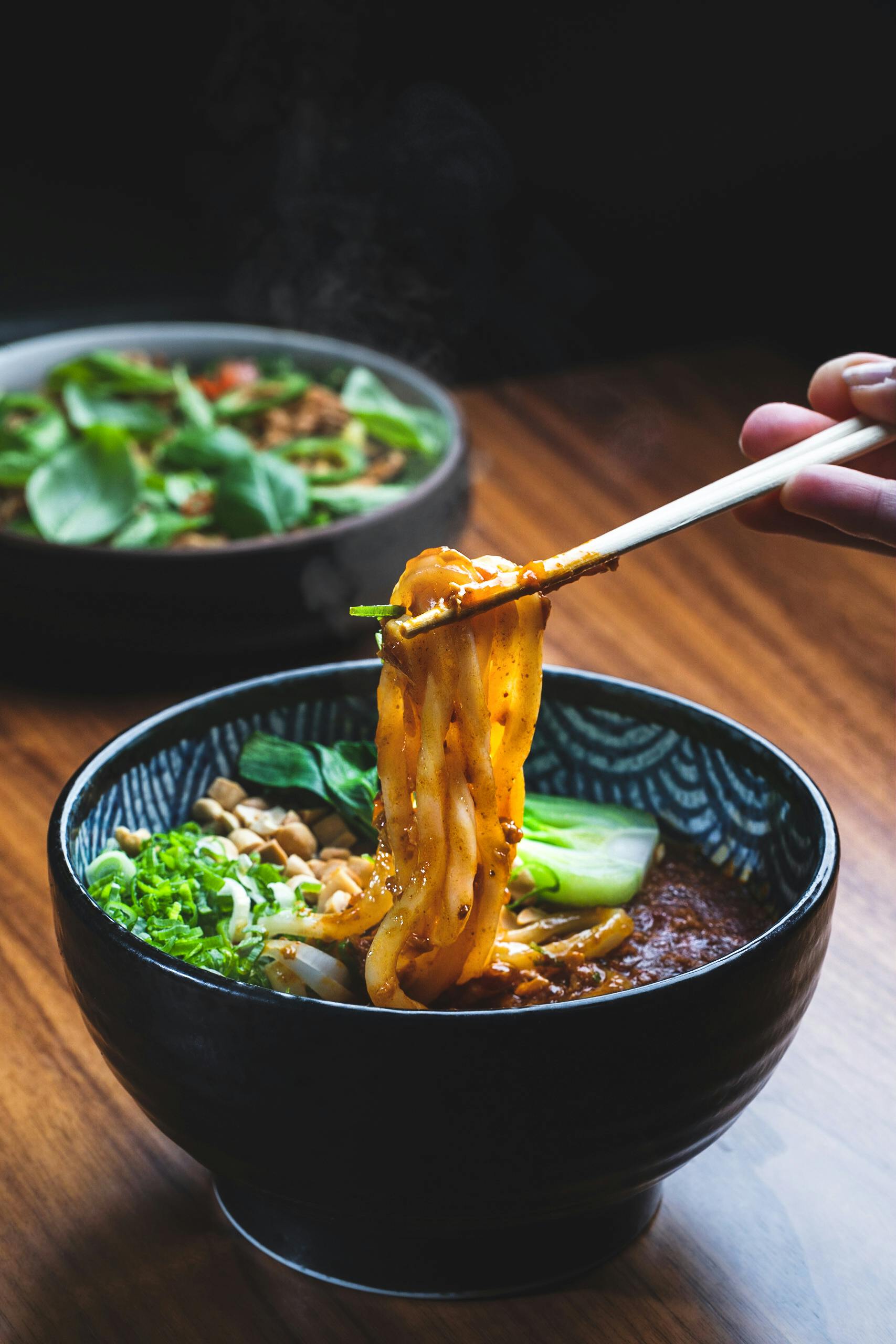 A steaming bowl of flavorful ramen garnished with fresh vegetables and nuts.