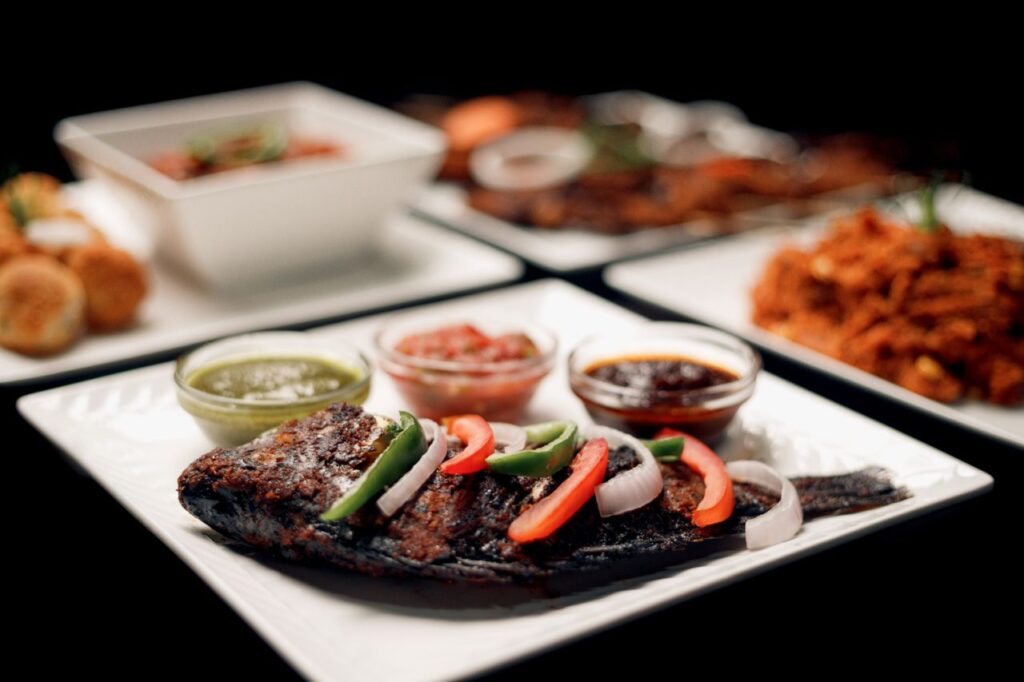 Delicious gourmet grilled fish served with assorted sauces and fresh vegetables on a square plate.