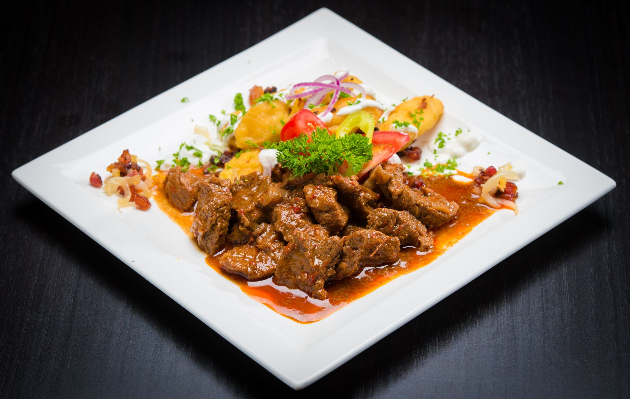 A savory beef stew served with colorful vegetables on a white plate.