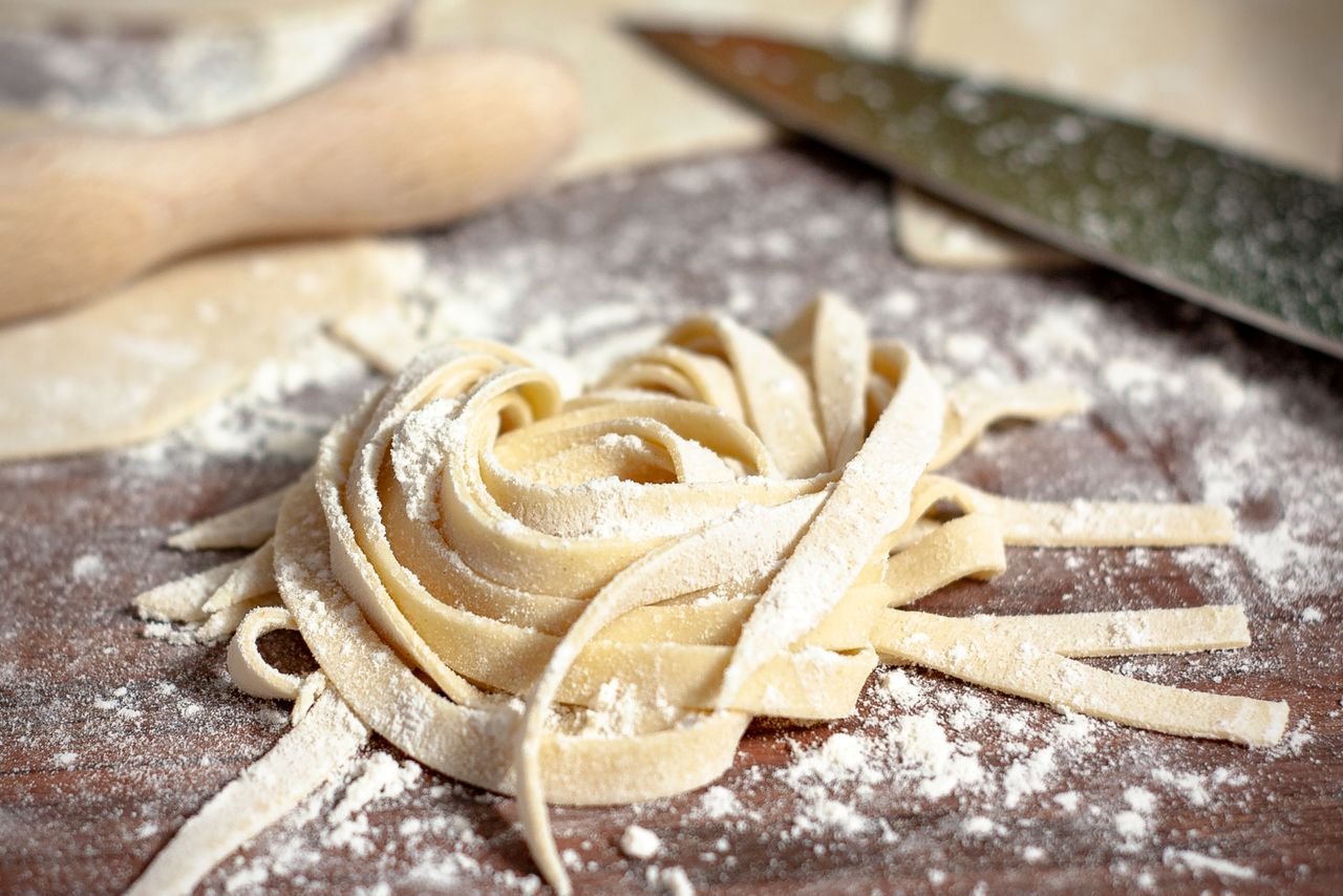 Close-up of freshly made tagliatelle pasta with flour on a wooden table, showcasing food preparation.