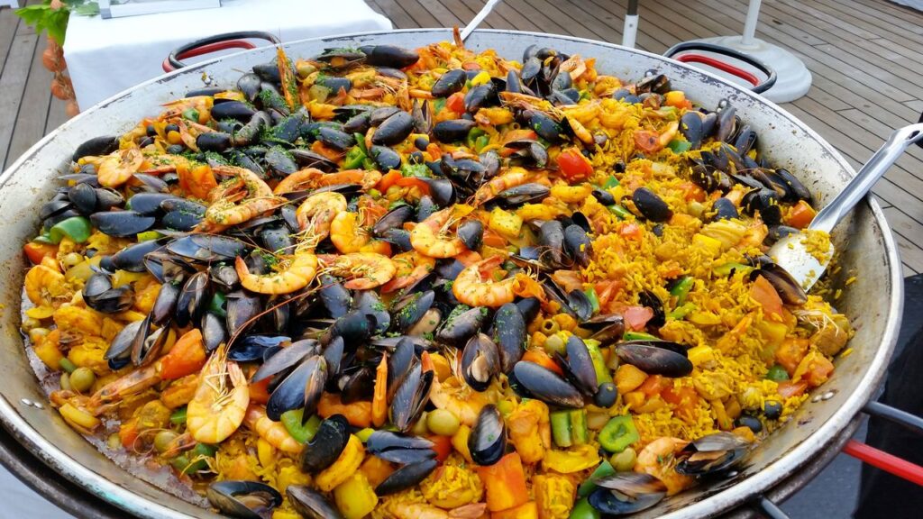 Close-up of a large pan of colorful seafood paella outdoors.