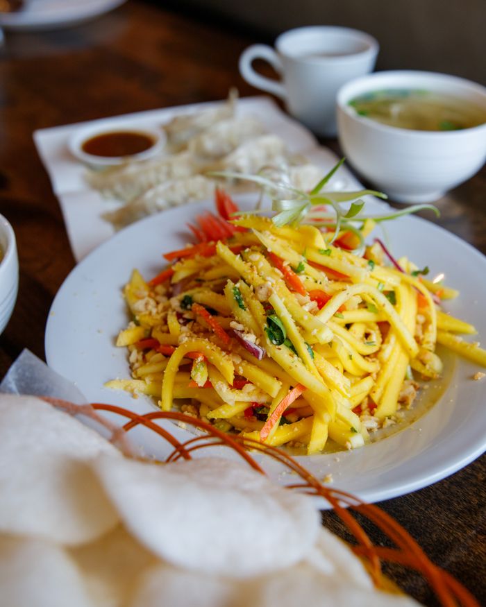 A colorful mango salad with Asian ingredients, garnished and served with tea, perfect for a vibrant meal.