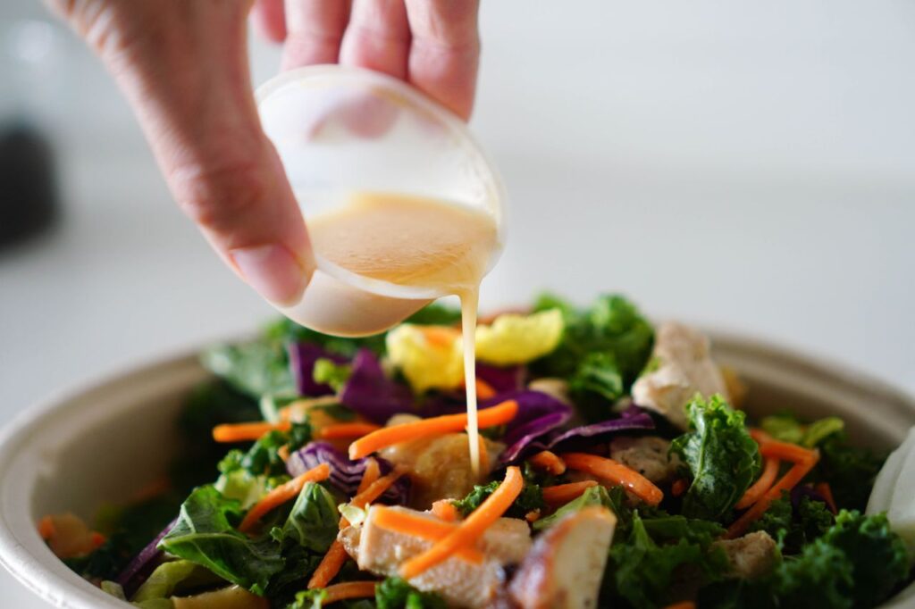 A delicious and healthy salad topped with fresh dressing being poured from a cup.